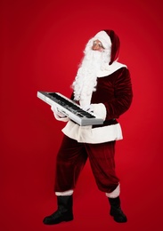 Photo of Santa Claus with synthesizer on red background. Christmas music