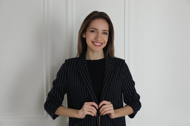 Portrait of beautiful young woman in fashionable suit near white wall. Business attire