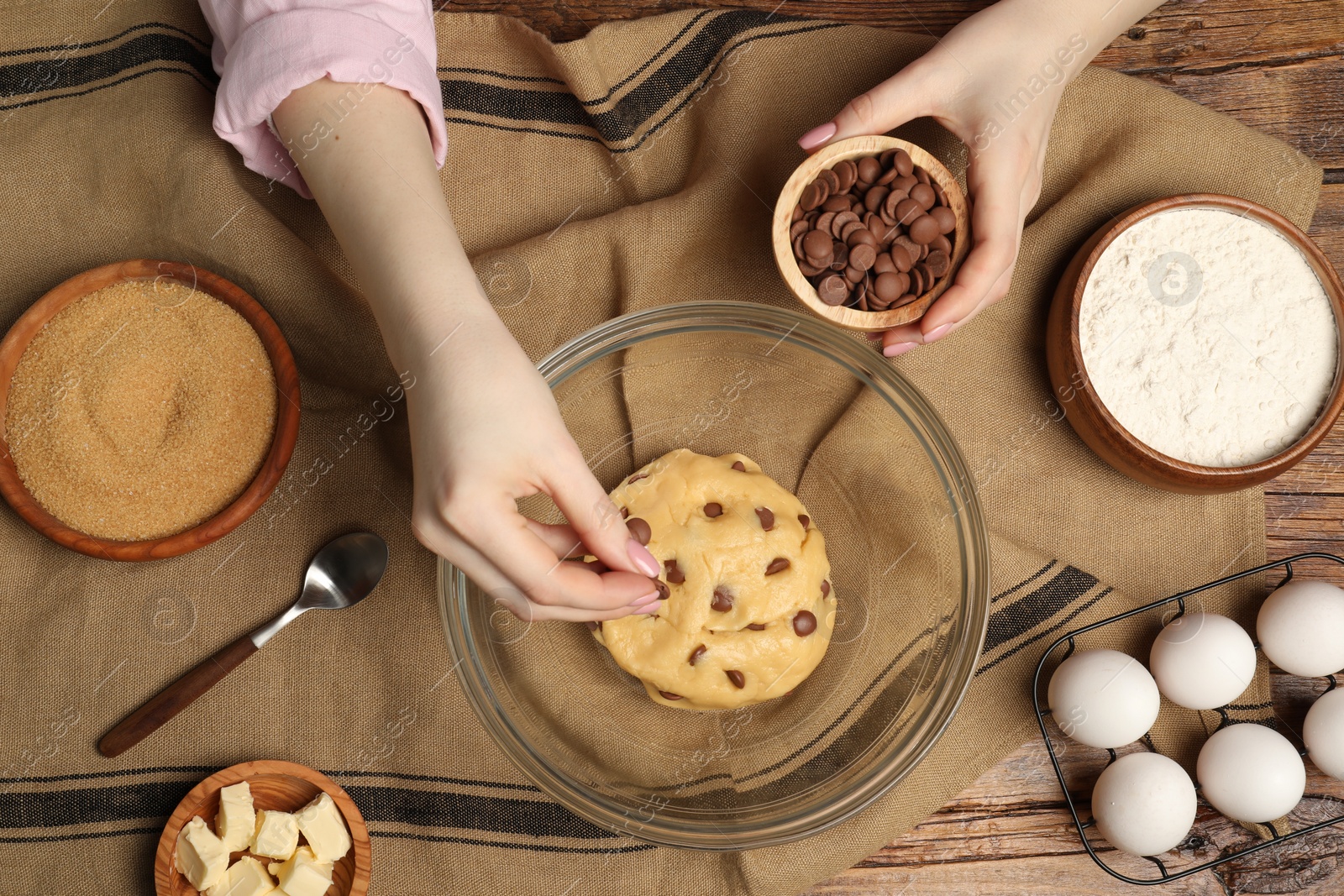 Photo of Cooking sweet cookies. Woman adding chocolate chips to dough at wooden table, top view