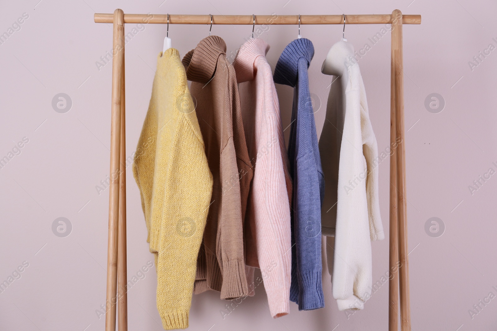 Photo of Warm sweaters hanging on wooden rack against pink background