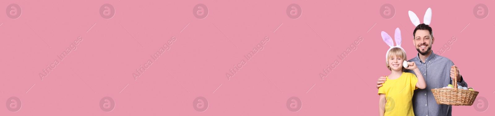 Image of Happy father and his son with bunny ears holding basket full of Easter eggs on pink background, space for text. Banner design