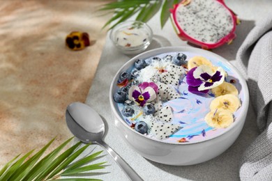 Photo of Delicious smoothie bowl with fresh fruits, blueberries and flowers served on color textured table. Space for text