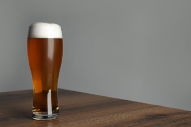 Photo of Glass of tasty dark beer on wooden table against grey background. Space for text