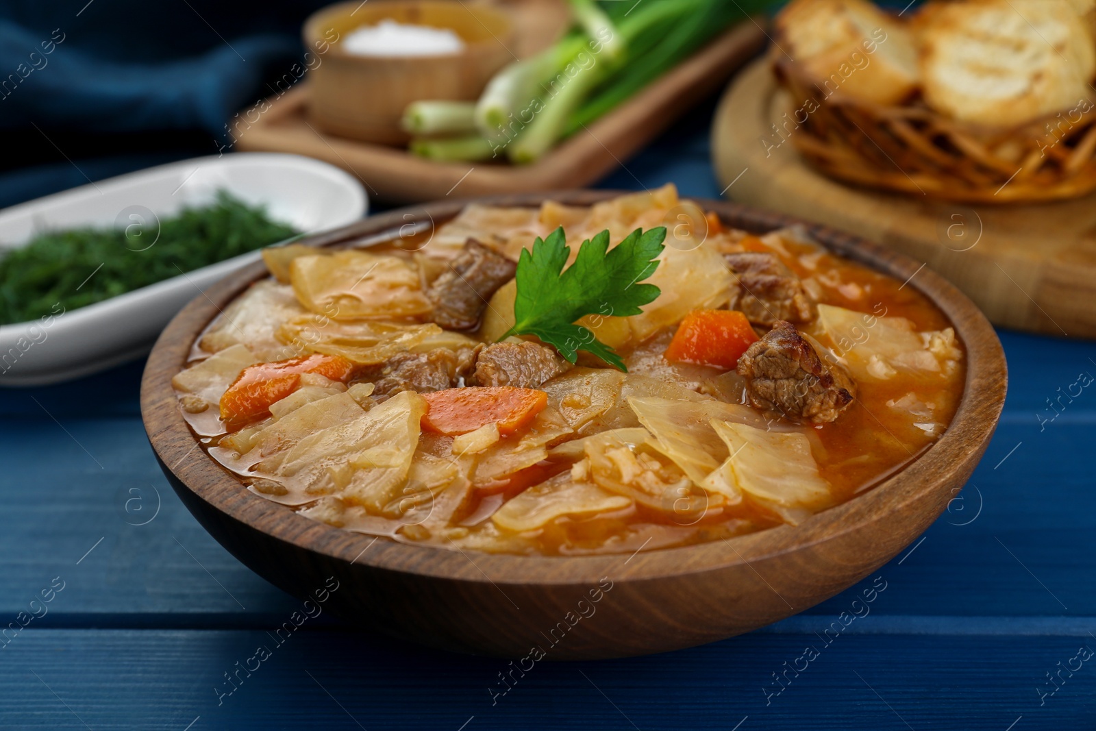 Photo of Tasty cabbage soup with meat, carrot and parsley on blue wooden table, closeup