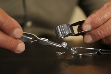 Photo of Professional jeweler working with beautiful ring at table, closeup
