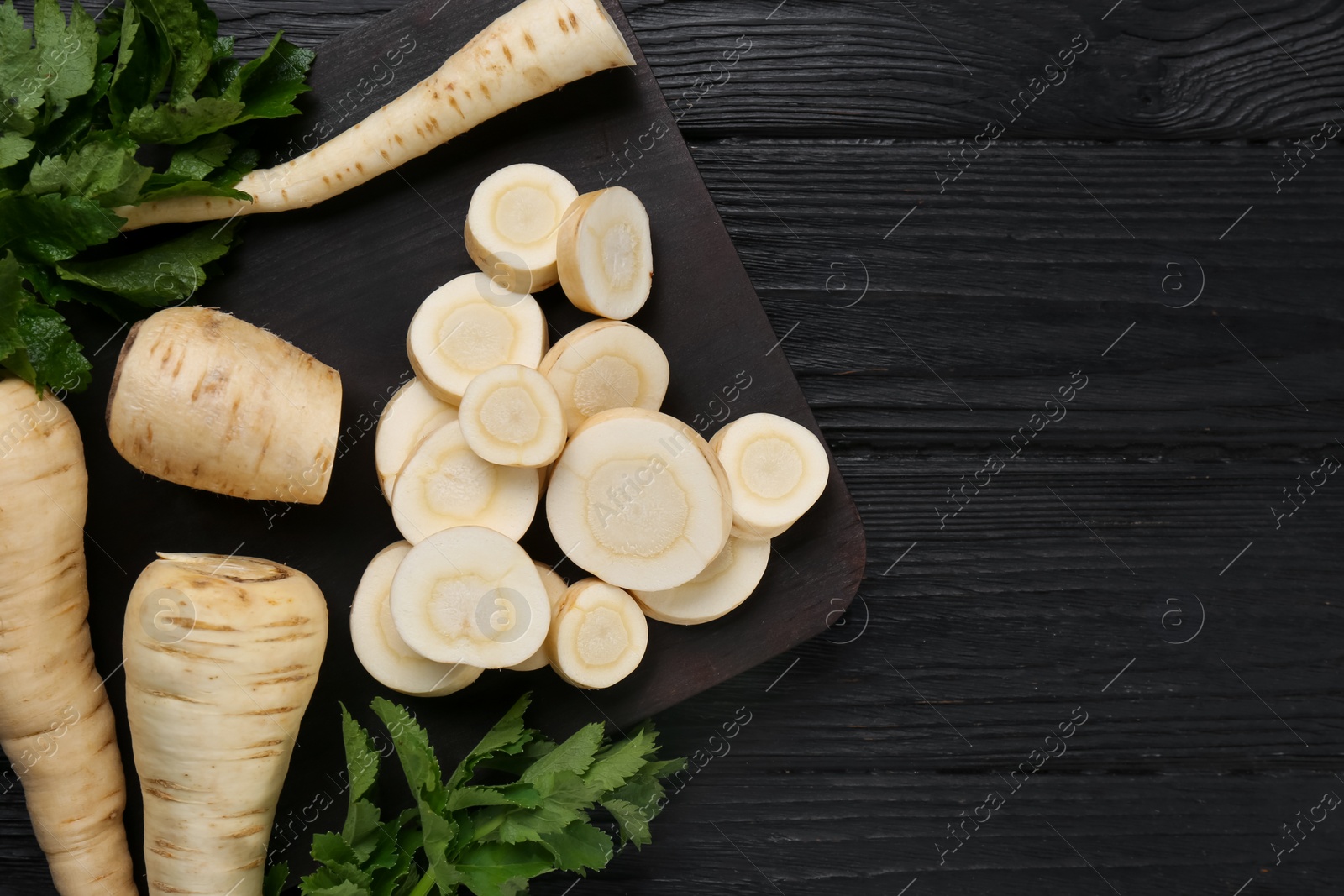 Photo of Whole and cut parsnips on black wooden table, flat lay. Space for text