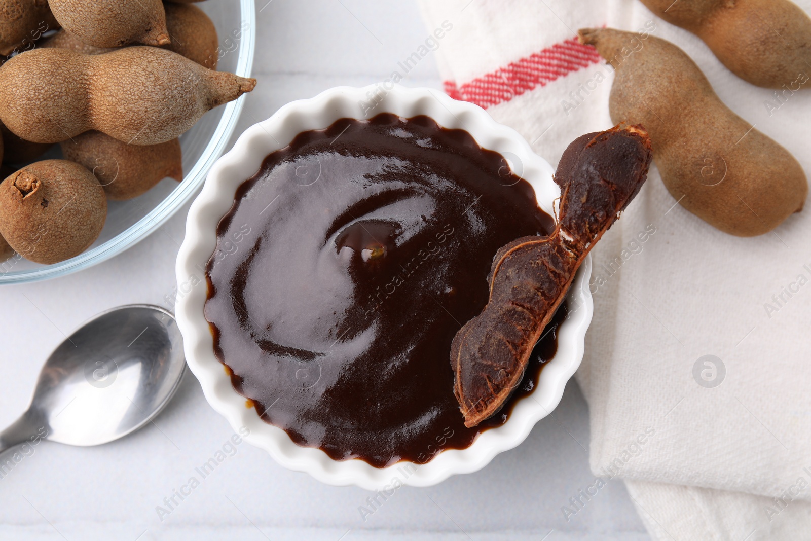 Bowl of tamarind sauce and fresh pods on white tiled table, flat lay Photo of Bowl of tamarind sauce and fresh pods on white tiled table, flat lay