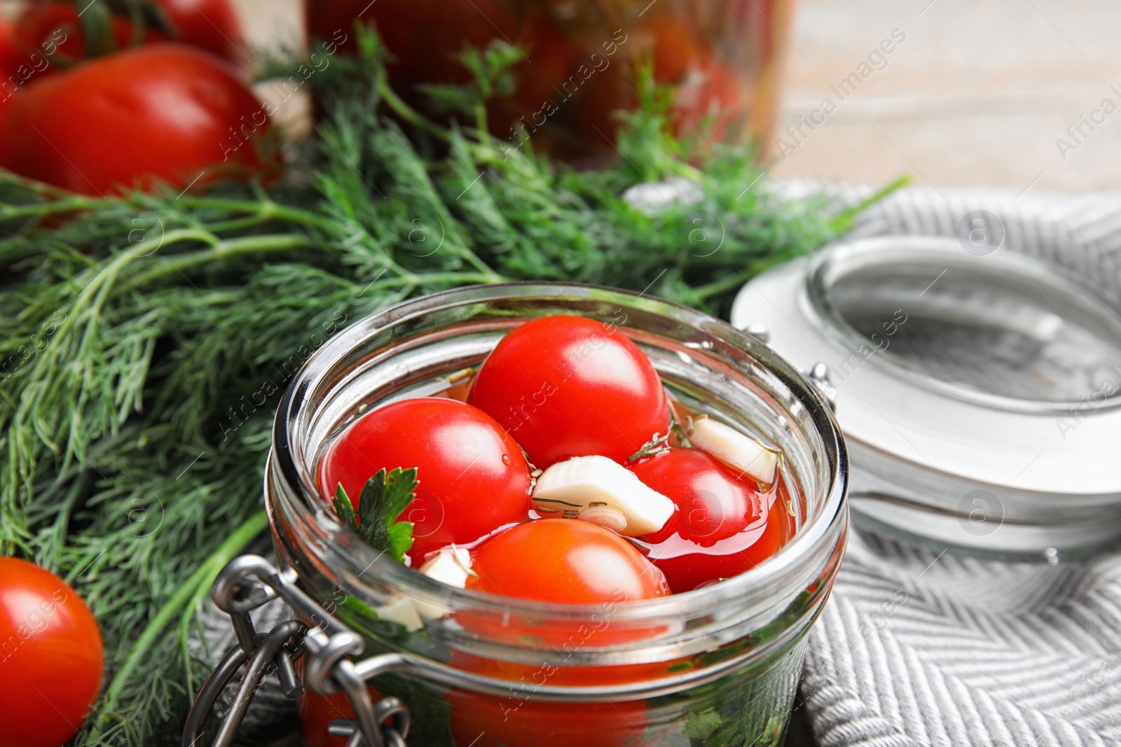 Photo of Pickled tomatoes in glass jar and products on table, closeup view