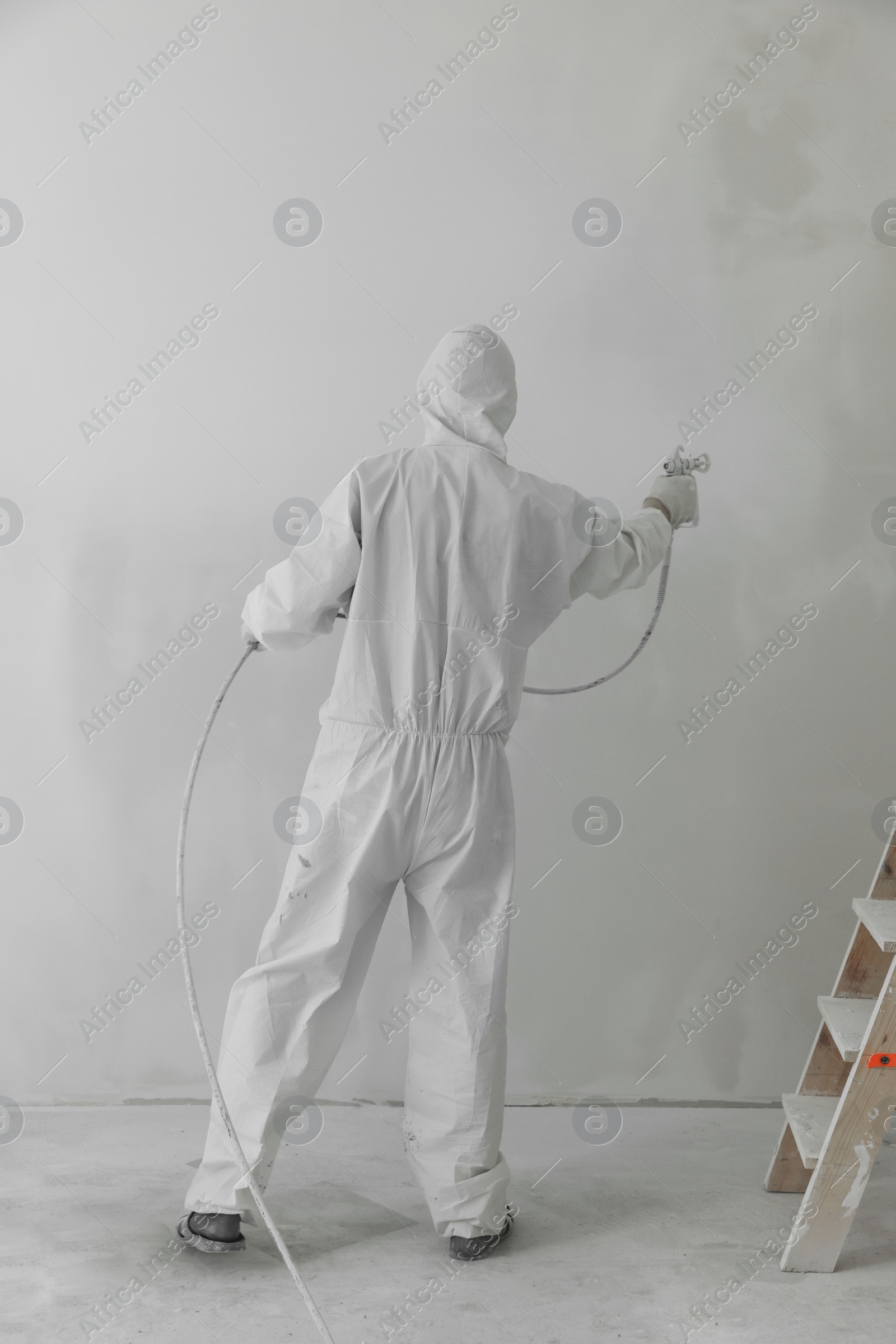 Photo of Decorator painting wall with spray indoors, back view