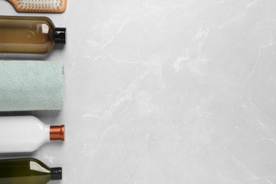 Shampoo bottles, hair brush and towel on grey table, flat lay. Space for text