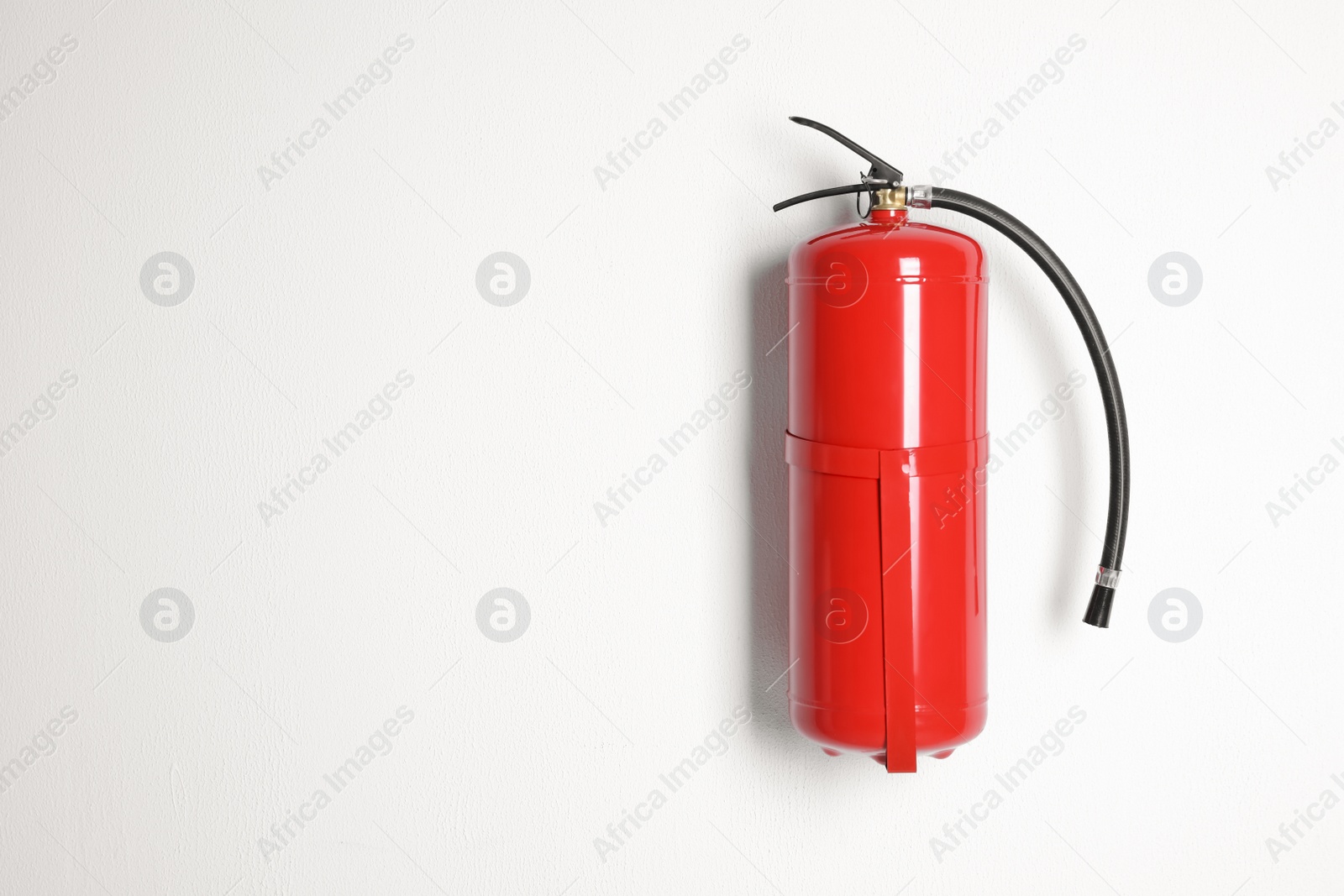 Photo of Fire extinguisher hanging on white wall. Space for text