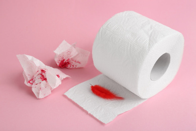 Photo of Roll of toilet paper and red feather on pink background. Hemorrhoid problems