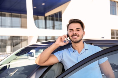 Photo of Young man talking on phone near modern car, outdoors