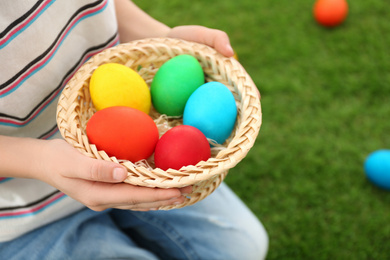 Photo of Cute little boy with basket full of Easter eggs outdoors, closeup