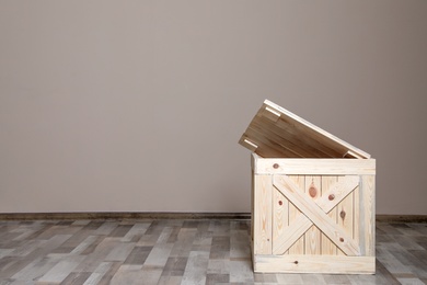 Photo of Wooden crate on floor at beige wall. Space for text