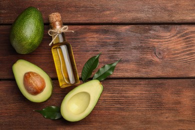 Photo of Glass bottle of cooking oil and fresh avocados on wooden table, flat lay. Space for text