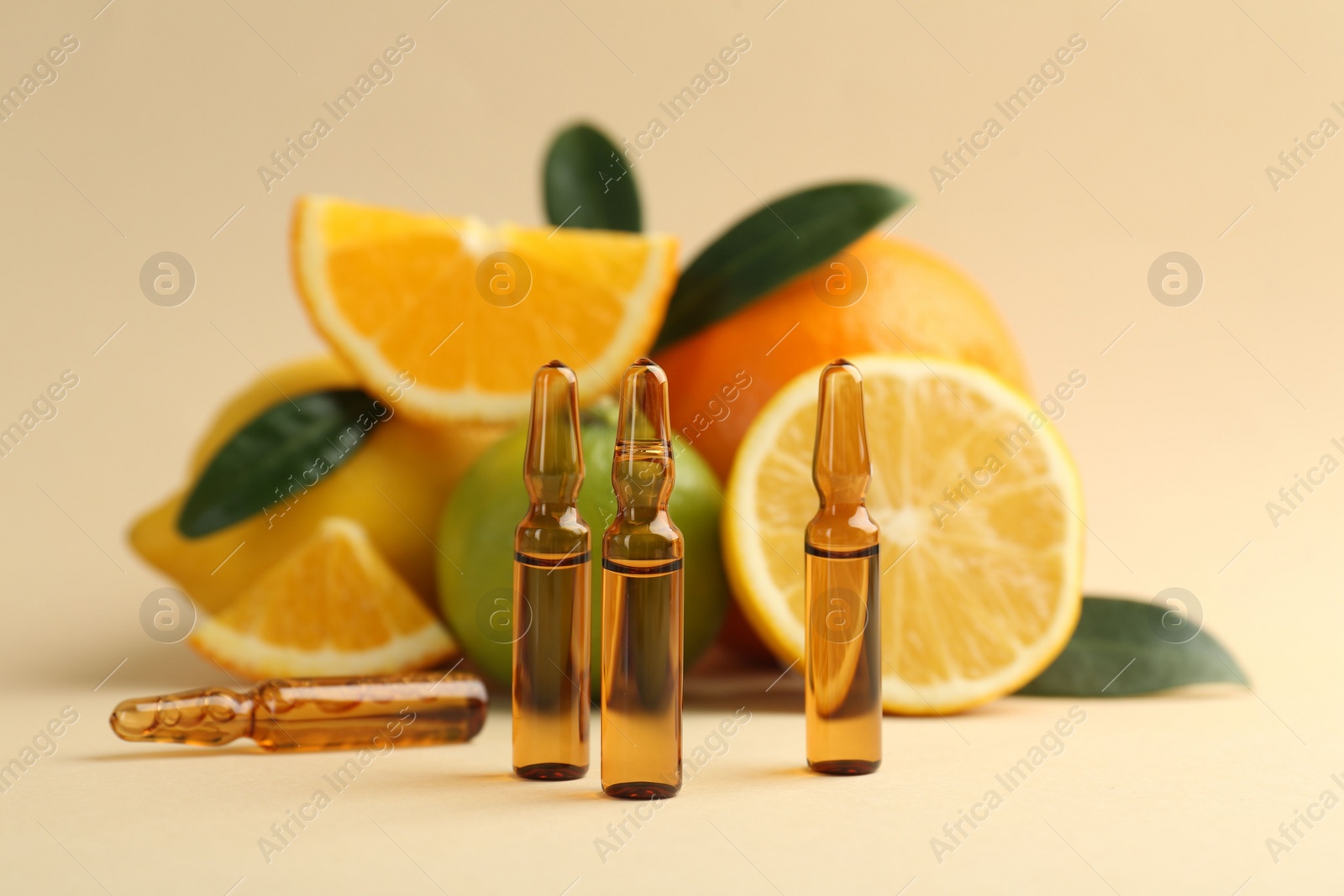 Photo of Skincare ampoules with vitamin C, different citrus fruits and leaves on beige background