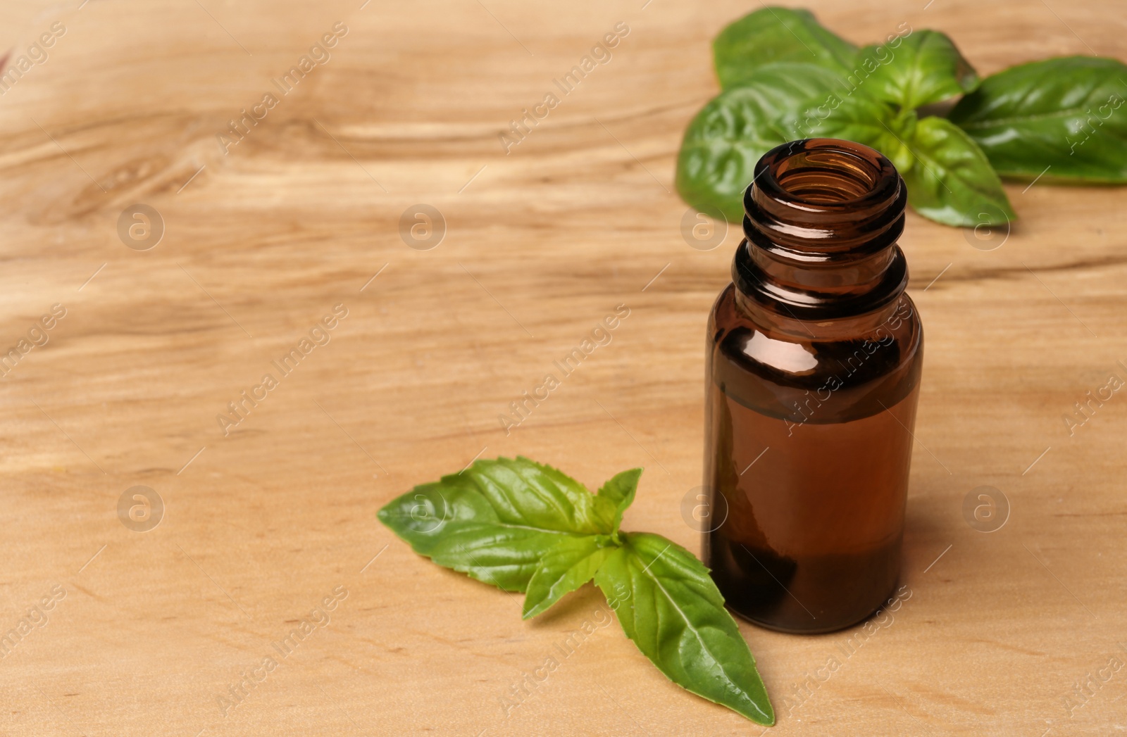 Photo of Bottle of basil essential oil and fresh leaves on wooden table. Space for text