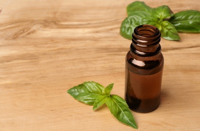 Bottle of basil essential oil and fresh leaves on wooden table. Space for text