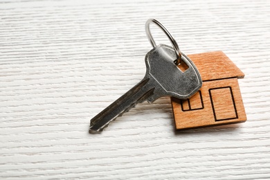 Photo of Key with trinket in shape of house on wooden background. Real estate agent services