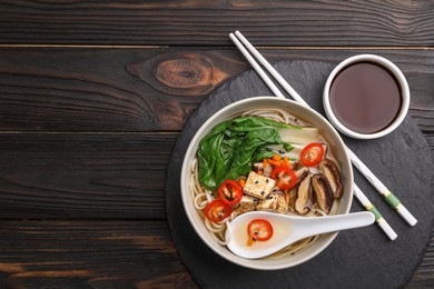 Bowl of vegetarian ramen served on dark wooden table, top view. Space for text