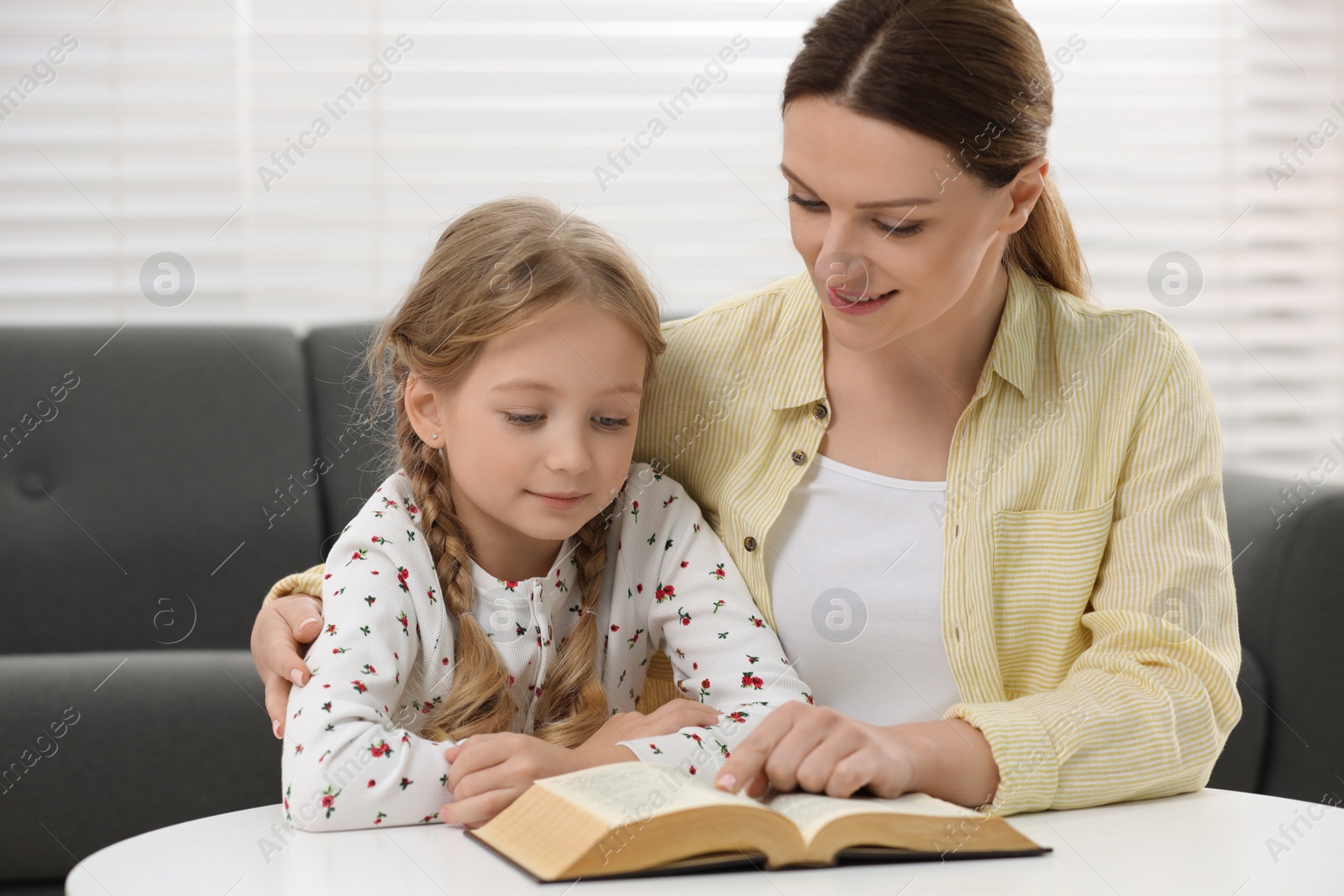 Photo of Girl and her godparent reading Bible together at table indoors