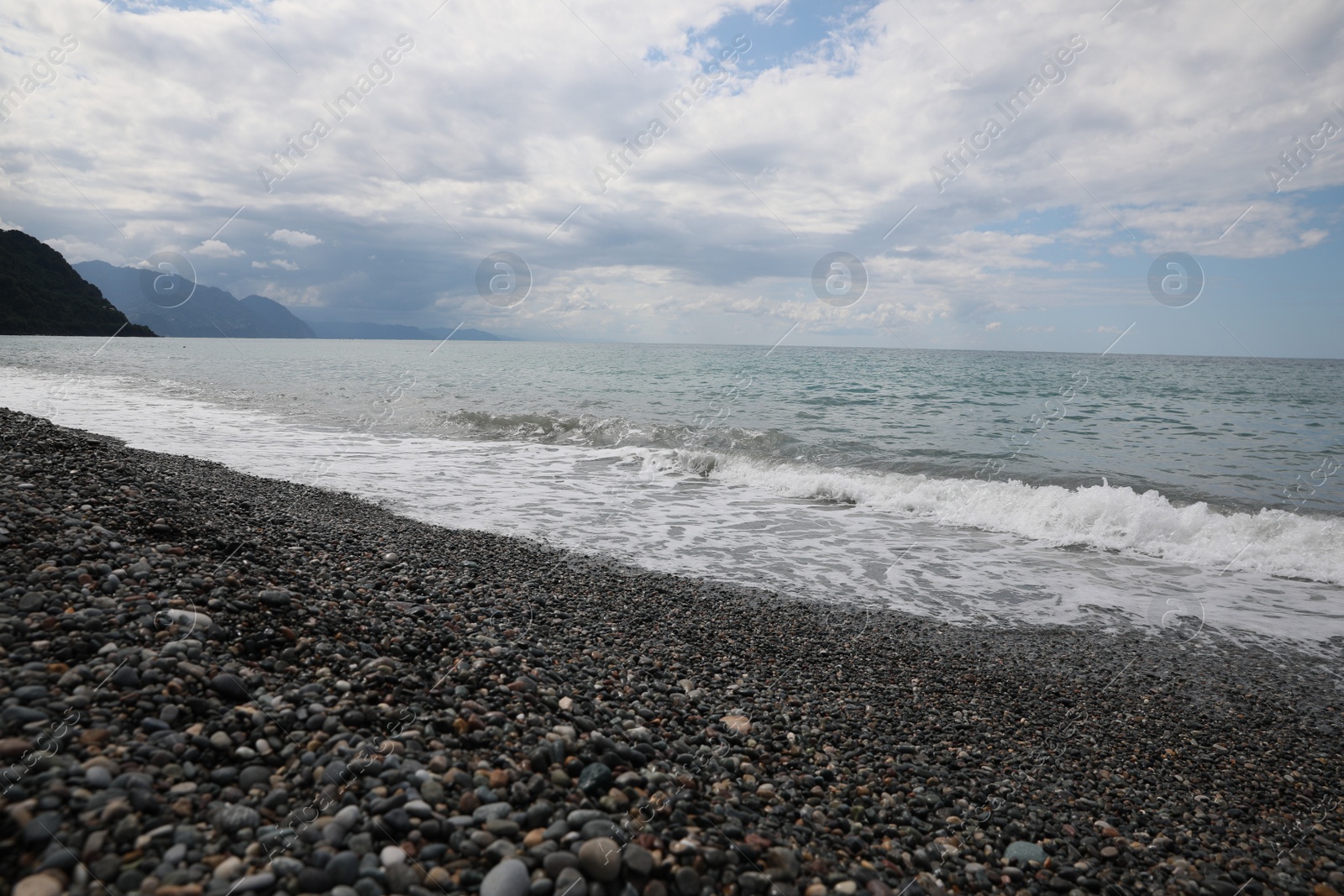 Photo of Picturesque view of beautiful sea shore and hills under sky with fluffy clouds