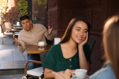 Jealous man spying on ex girlfriend in outdoor cafe