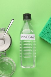 Photo of Eco friendly natural cleaners. Vinegar in bottle, sponge and jar of soda on green background, flat lay