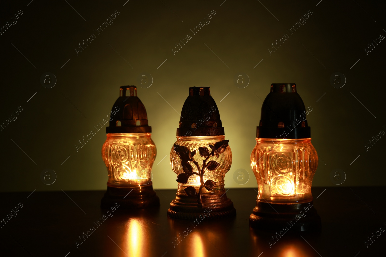 Photo of Beautiful glowing grave lights on table in darkness. Symbol of remembrance