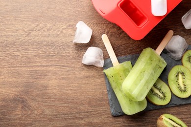 Photo of Tasty kiwi ice pops and space for text on wooden table, flat lay. Fruit popsicle