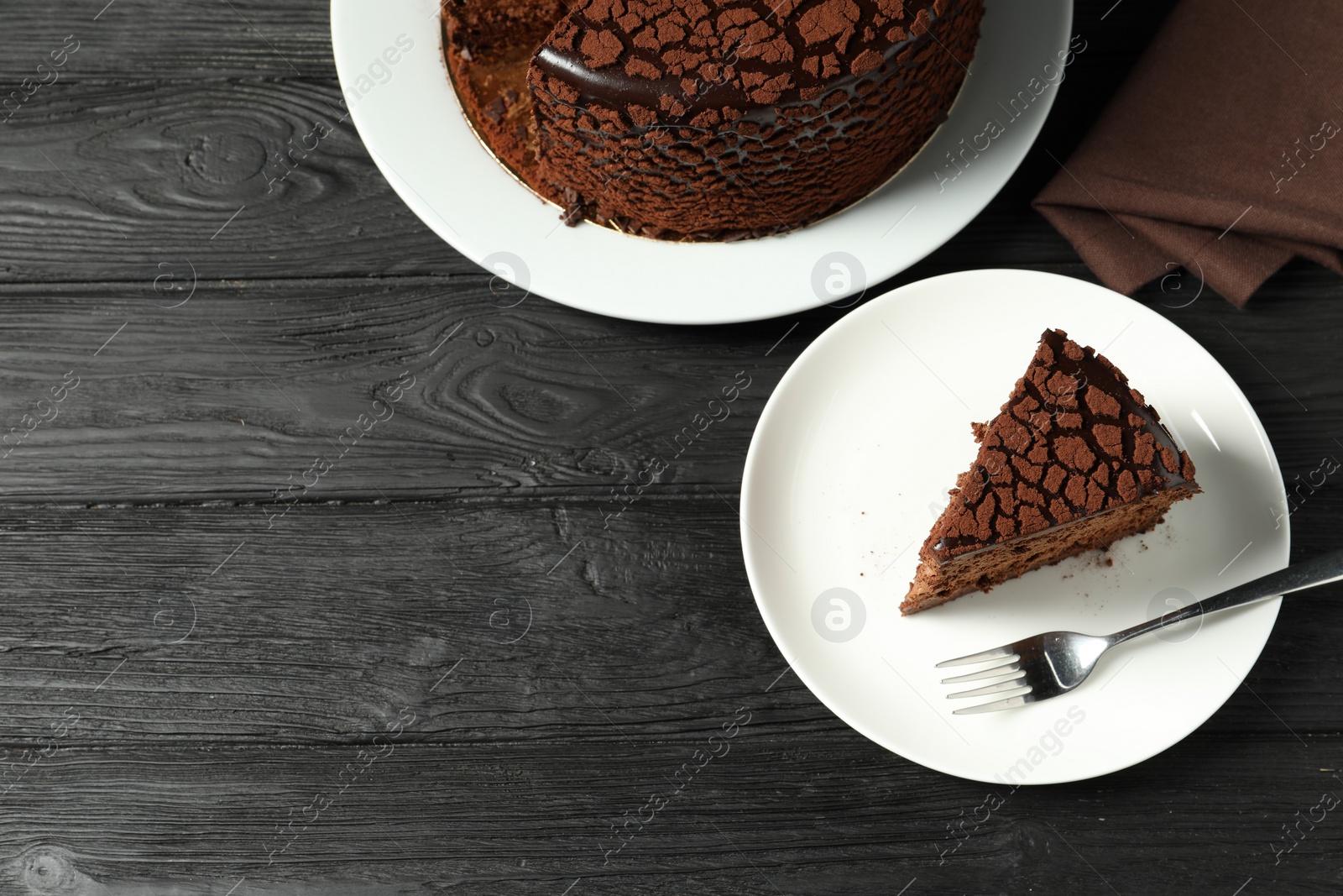 Photo of Piece of delicious chocolate truffle cake and fork on black wooden table, top view. Space for text