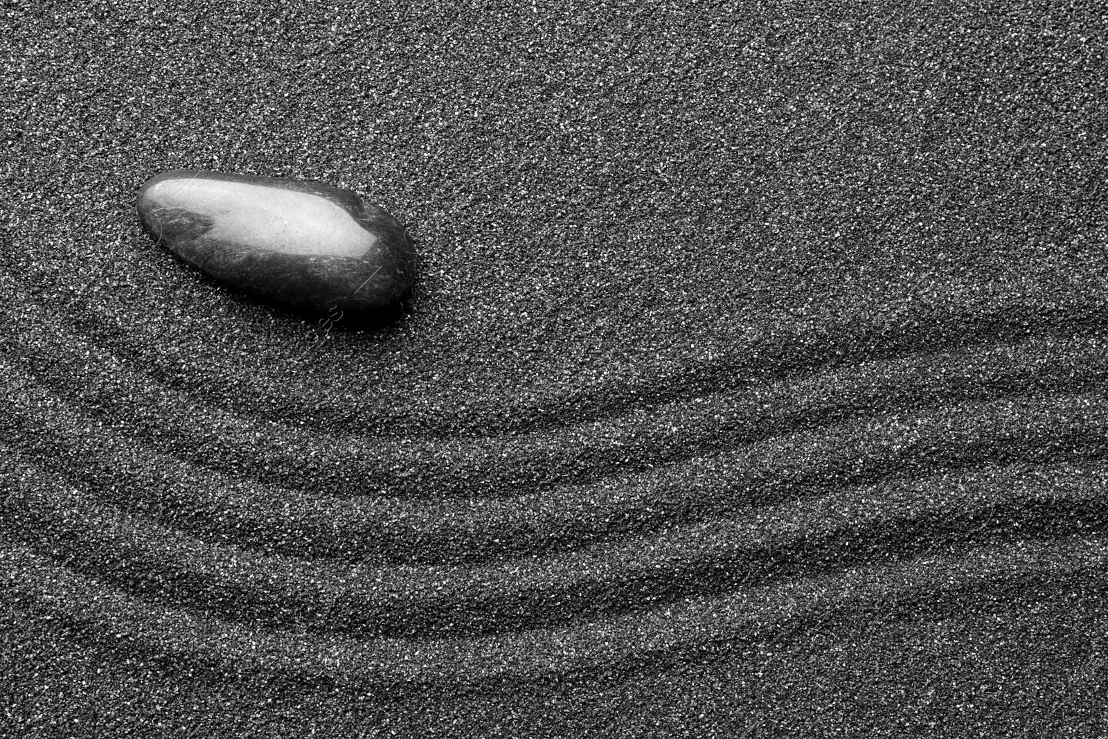 Photo of Zen garden stone on black sand with pattern, top view