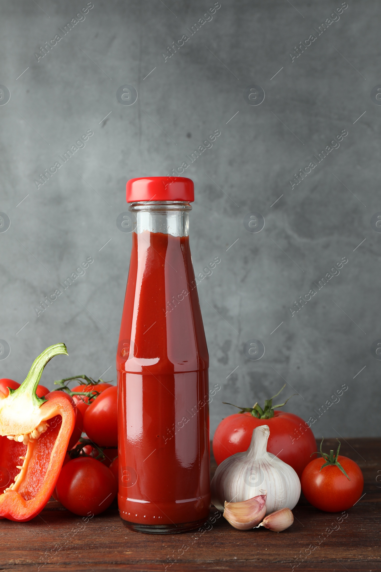 Photo of Bottle of tasty ketchup and ingredients on wooden table