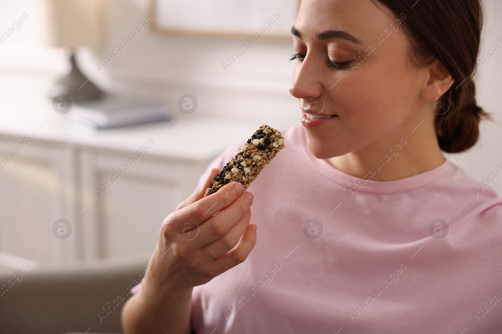 Photo of Woman eating tasty granola bar at home