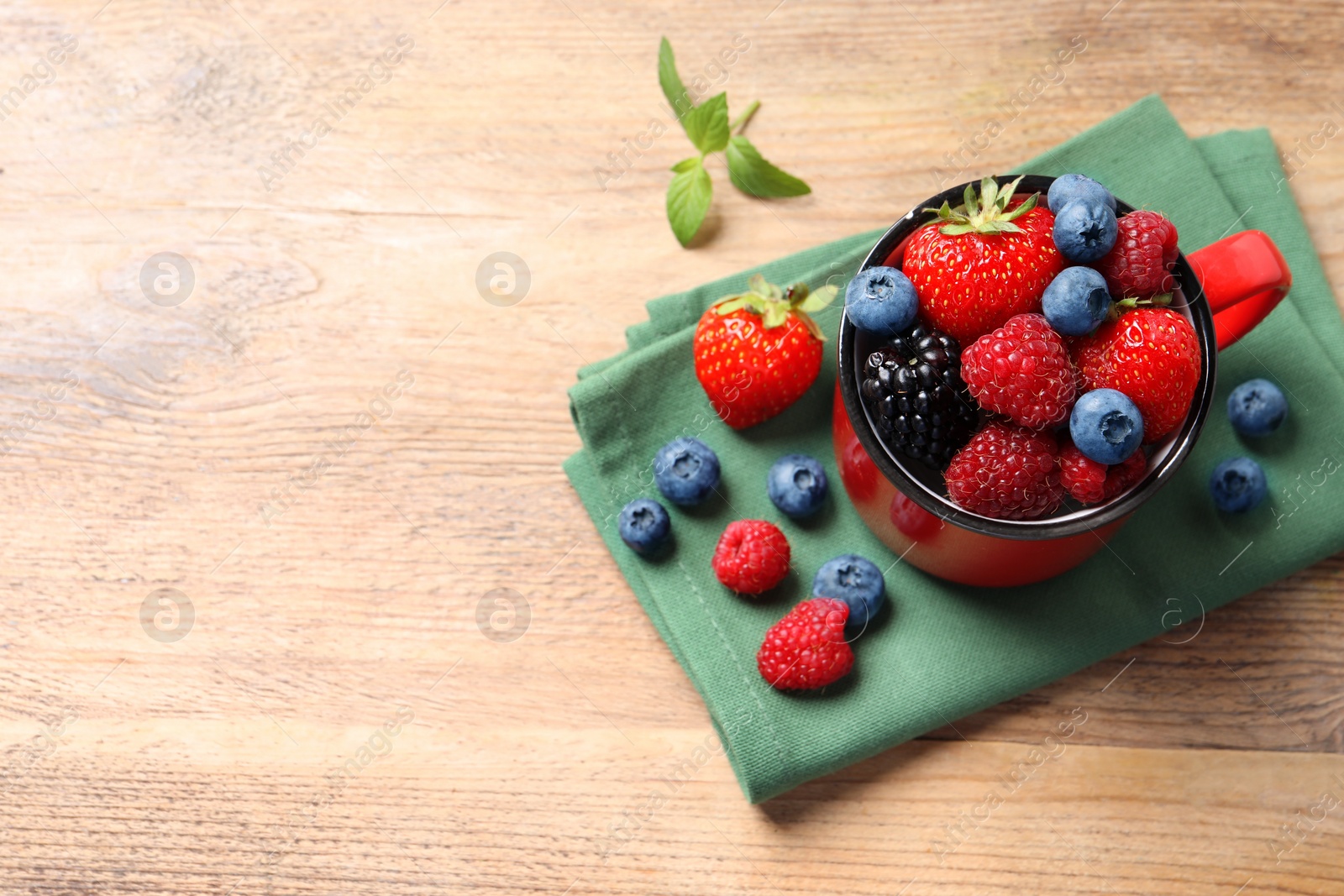 Photo of Many different fresh ripe berries in mug on wooden table, above view. Space for text