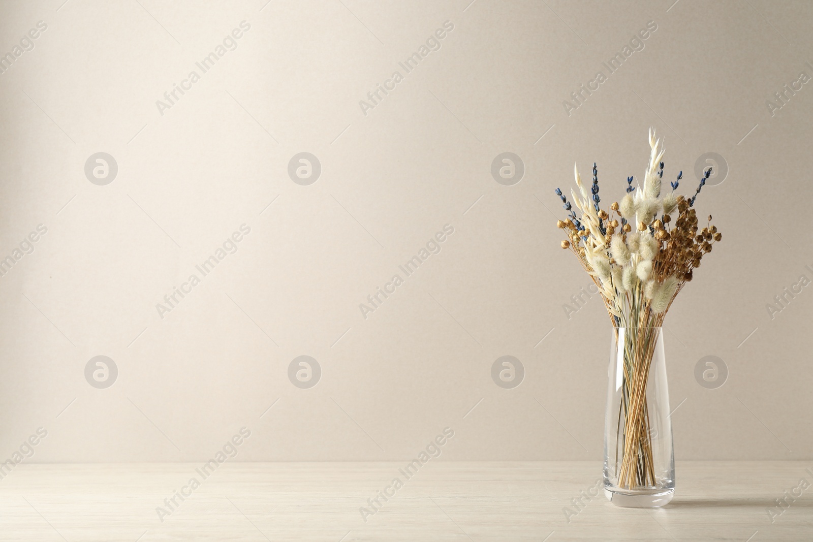 Photo of Dried flowers in vase on table against light background. Space for text