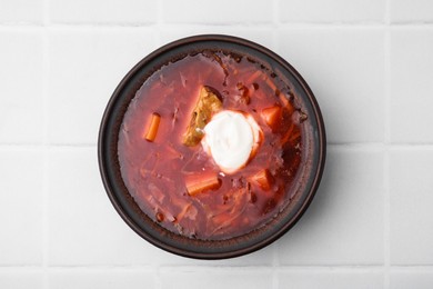 Tasty borscht with sour cream in bowl on white tiled table, top view