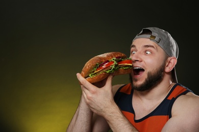 Young man eating tasty burger on color background. Space for text