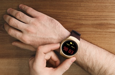Man measuring oxygen level with smartwatch at wooden table, top view