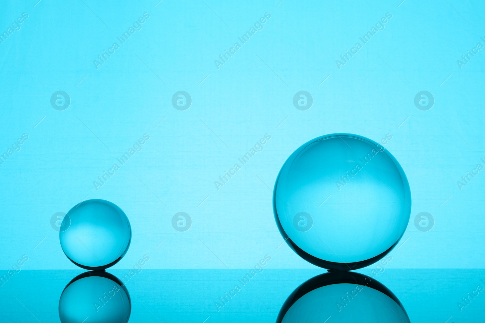 Photo of Transparent glass balls on mirror surface against turquoise background. Space for text