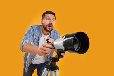 Surprised astronomer with telescope on orange background