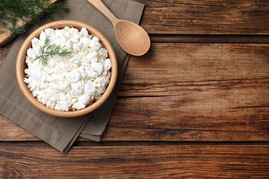 Photo of Fresh cottage cheese with dill in bowl on wooden table, flat lay. Space for text