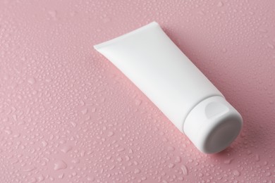 Moisturizing cream in tube on pink background with water drops, closeup. Space for text