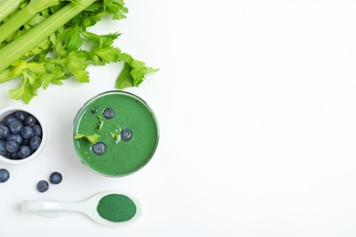 Glass of spirulina smoothie, berries, celery and spoon with powder on white background, top view