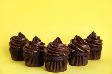 Delicious chocolate cupcakes with cream on yellow background. Space for text