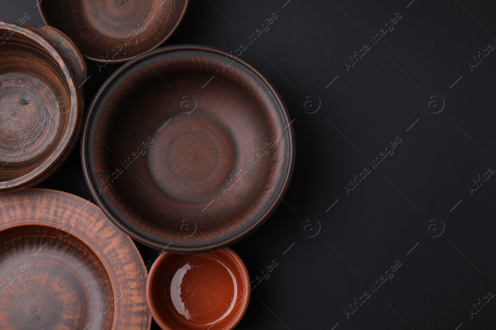 Photo of Bowls and plates on black background, flat lay. Space for text