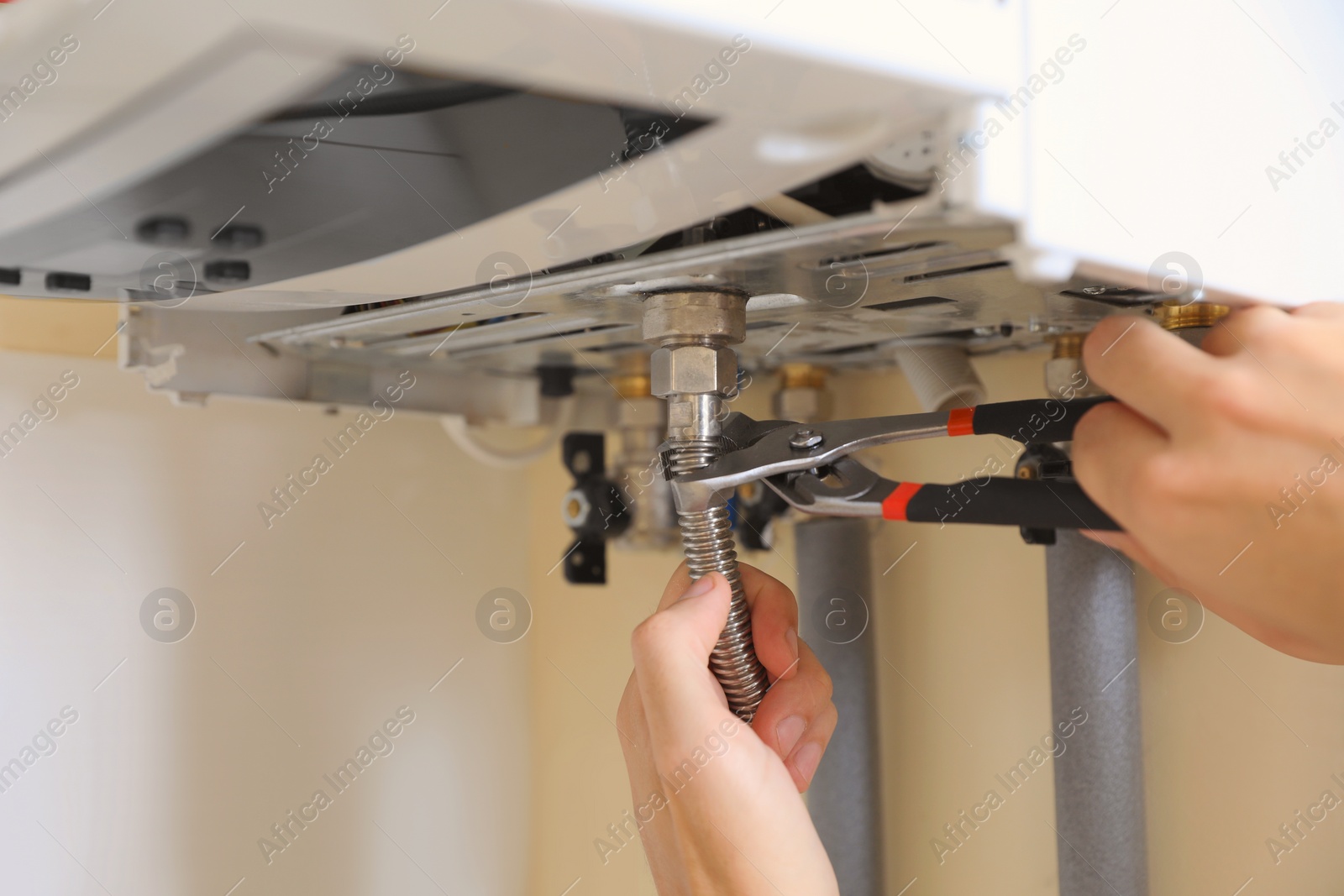 Photo of Man repairing gas boiler with waterpump plier indoors, closeup