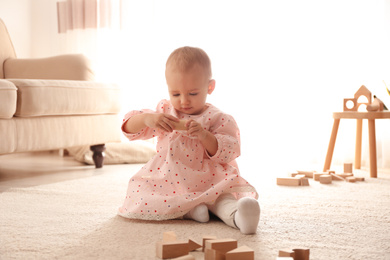 Photo of Cute child playing with wooden building blocks on floor at home