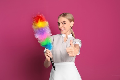 Young chambermaid with dusting brush on color background